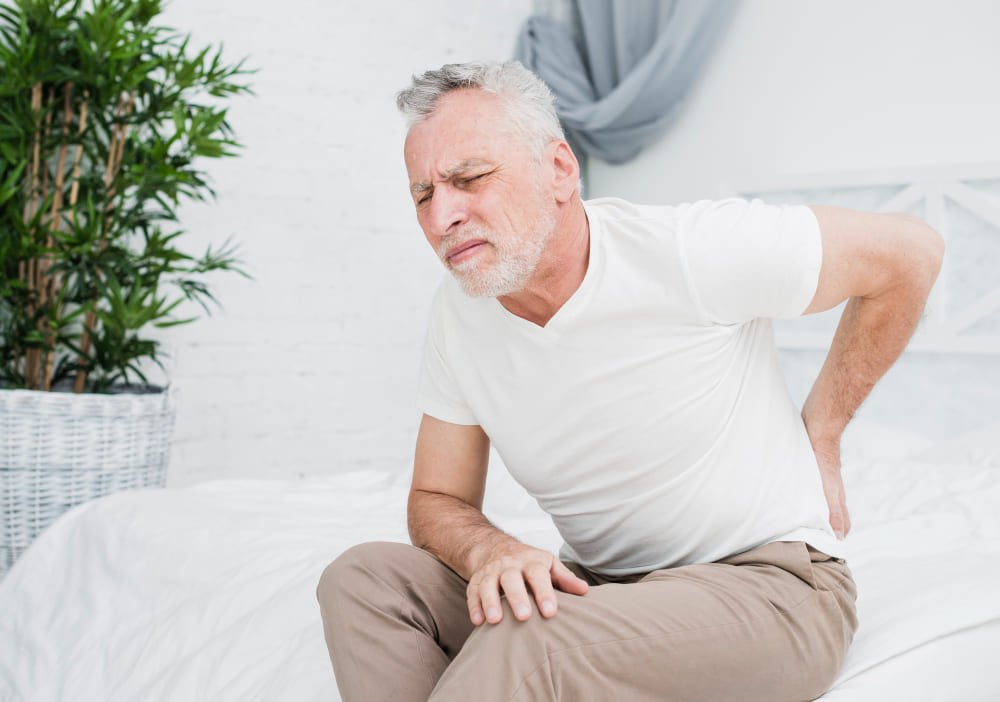 hombre mayor sentado en sofa con expresion de dolor en espalda lumbar problemas musculares